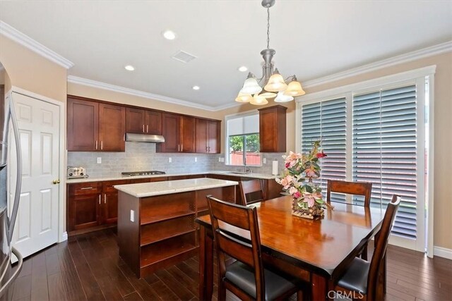 7509 Woodstream Ct, Rancho Cucamonga, CA 91739 - kitchen featuring under cabinet range hood, a chandelier, dark wood-style flooring, decorative backsplash, and ornamental molding