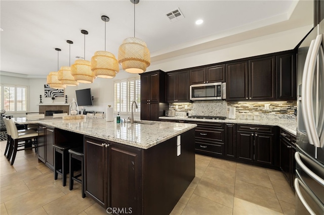 43875 Spiaggia Pl, Indio, CA 92203 - kitchen with appliances with stainless steel finishes, decorative backsplash, a large island with sink, light stone counters, and a breakfast bar area