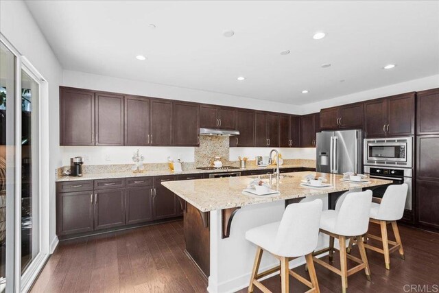 7147 Sitio Bahia, Carlsbad, CA 92009 - kitchen with stainless steel appliances, a kitchen breakfast bar, a kitchen island with sink, dark wood finished floors, and light stone counters