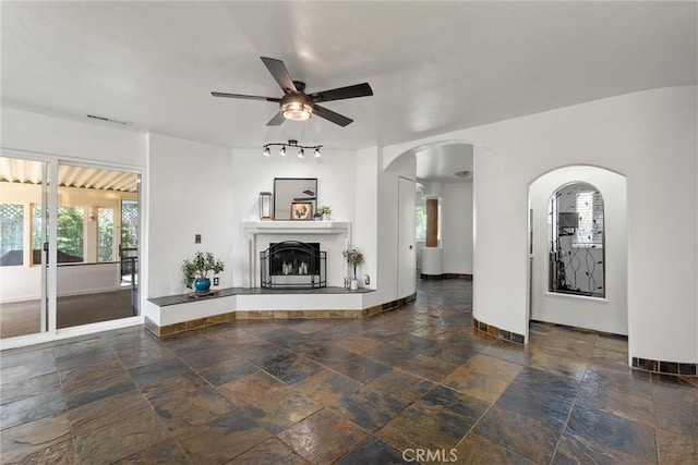2427 Ceanothus Ave, Chico, CA 95926 - unfurnished living room with stone tile floors, a ceiling fan, a fireplace with raised hearth, and arched walkways
