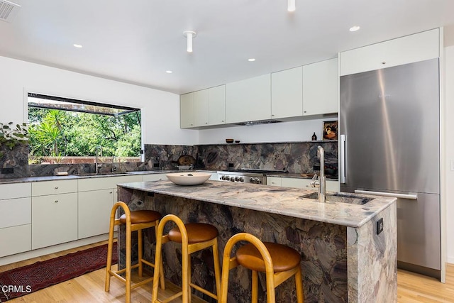 808 Inverness Dr, La Canada Flintridge, CA 91011 - kitchen featuring freestanding refrigerator, a breakfast bar area, light wood finished floors, white cabinetry, and a kitchen island with sink