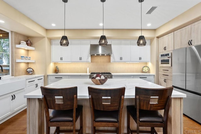 7661 Sitio Algodon, Carlsbad, CA 92009 - kitchen featuring stainless steel appliances, wall chimney exhaust hood, a center island, tasteful backsplash, and wood finished floors