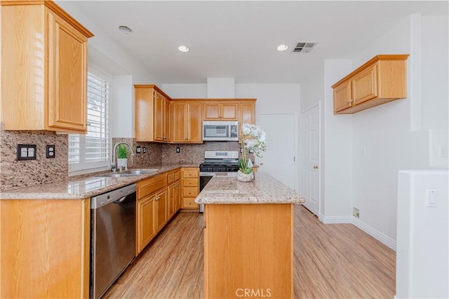 24646 Maple Ln, Harbor City, CA 90710 - kitchen featuring appliances with stainless steel finishes, light wood-style flooring, a kitchen island, tasteful backsplash, and light stone counters