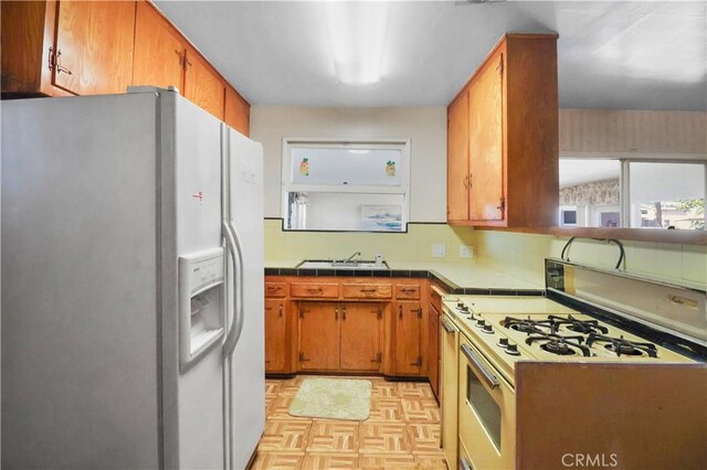 8707 Chester St, Paramount, CA 90723 - kitchen featuring white appliances, tile counters, brown cabinets, and backsplash