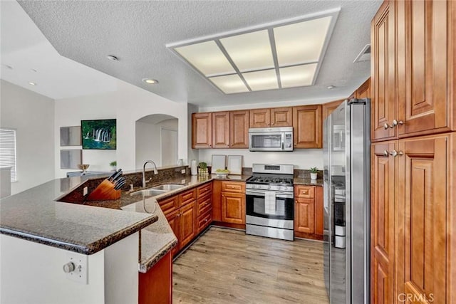 3433 E White Chapel Ct Unit F, Orange, CA 92869 - kitchen featuring stainless steel appliances, arched walkways, brown cabinetry, a peninsula, and light wood finished floors