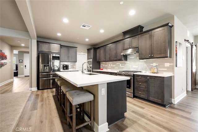 24420 Crooked Trail Dr, Menifee, CA 92584 - kitchen with stainless steel appliances, under cabinet range hood, dark brown cabinetry, backsplash, and a center island with sink
