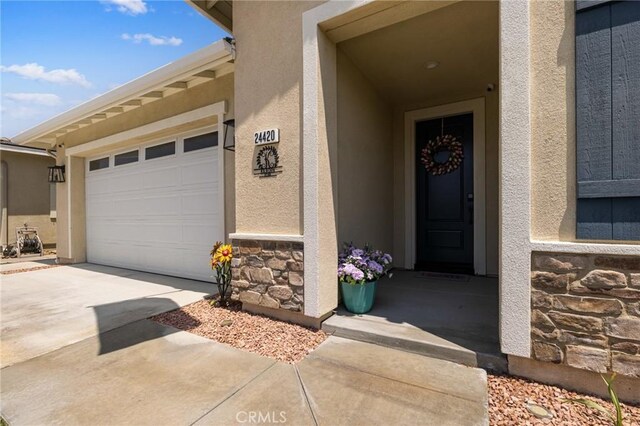 24420 Crooked Trail Dr, Menifee, CA 92584 - entrance to property with stone siding, driveway, stucco siding, and an attached garage