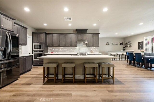 24420 Crooked Trail Dr, Menifee, CA 92584 - kitchen with stainless steel appliances, under cabinet range hood, light countertops, backsplash, and a kitchen breakfast bar
