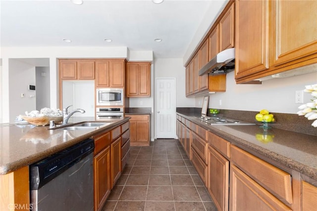 30315 Laruns St, Murrieta, CA 92563 - kitchen with appliances with stainless steel finishes, under cabinet range hood, dark tile patterned flooring, brown cabinets, and dark stone counters