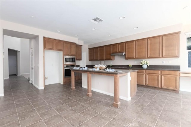 30315 Laruns St, Murrieta, CA 92563 - kitchen with appliances with stainless steel finishes, dark countertops, light tile patterned floors, recessed lighting, and an island with sink