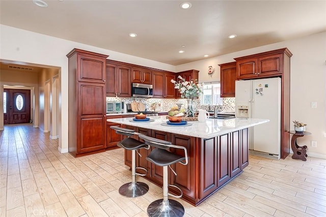 335 E Francis Ave, La Habra, CA 90631 - kitchen featuring stainless steel microwave, white fridge with ice dispenser, light wood-style flooring, decorative backsplash, and recessed lighting