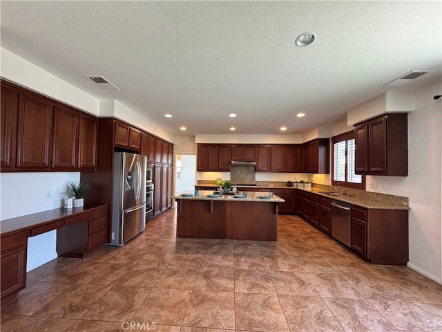 33314 Lazurite Way, Menifee, CA 92584 - kitchen with appliances with stainless steel finishes, a kitchen island, stone counters, built in desk, and a textured ceiling
