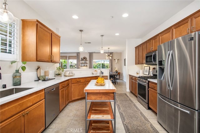 36287 Grazia Way, Winchester, CA 92596 - kitchen featuring appliances with stainless steel finishes, a peninsula, light countertops, brown cabinets, and hanging light fixtures