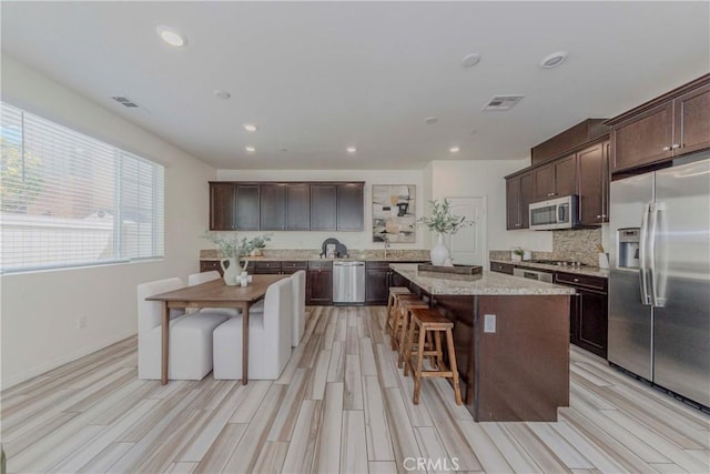 8708 Celebration St, Chino, CA 91708 - kitchen with stainless steel appliances, dark brown cabinetry, a center island, a breakfast bar area, and light wood-style floors