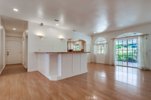 9733 Kentland Ave, Chatsworth, CA 91311 - kitchen with light wood-style flooring, arched walkways, a peninsula, stone counters, and recessed lighting