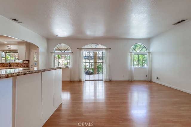 9733 Kentland Ave, Chatsworth, CA 91311 - kitchen featuring light wood finished floors, plenty of natural light, arched walkways, a textured ceiling, and white cabinetry