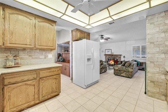 25270 Tradewinds Dr, Menifee, CA 92585 - kitchen with white fridge with ice dispenser, a ceiling fan, a brick fireplace, light tile patterned flooring, and light countertops