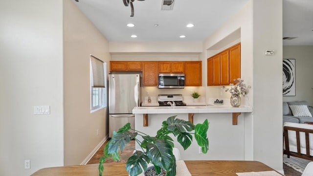 534 64th St, San Diego, CA 92114 - kitchen with appliances with stainless steel finishes, tile countertops, brown cabinetry, a peninsula, and recessed lighting