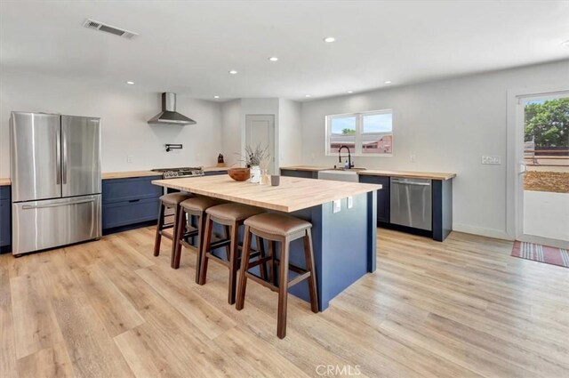 1500 Pacific Ave, Norco, CA 92860 - kitchen featuring stainless steel appliances, wall chimney range hood, butcher block counters, a breakfast bar, and light wood-style floors