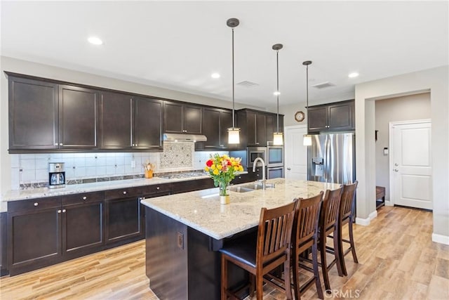44655 Howell Mountain St, Temecula, CA 92592 - kitchen with under cabinet range hood, dark brown cabinetry, light stone countertops, decorative backsplash, and hanging light fixtures