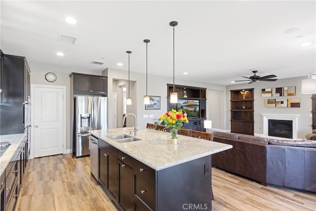 44655 Howell Mountain St, Temecula, CA 92592 - kitchen with stainless steel appliances, a ceiling fan, a glass covered fireplace, light stone counters, and light wood-type flooring