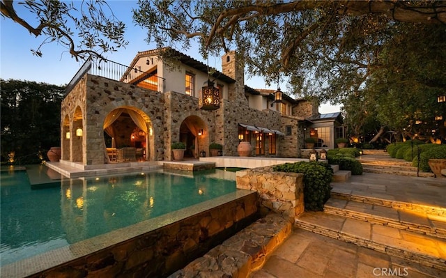 36 Pelican Crest Dr, Newport Coast, CA 92657 - back of property featuring stone siding, a patio, a chimney, and an infinity pool