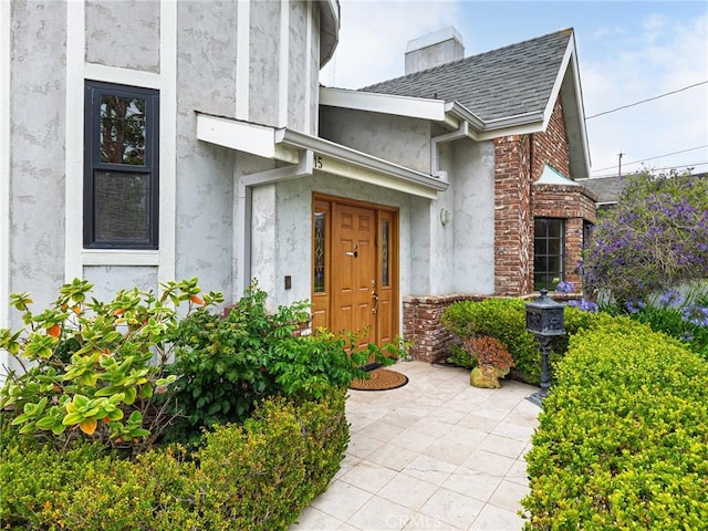 715 W Palm Ave, El Segundo, CA 90245 - view of exterior entry featuring stucco siding, brick siding, roof with shingles, and a chimney
