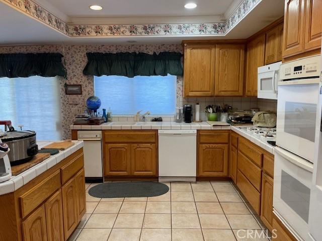 18759 Mayall St, Northridge, CA 91324 - kitchen with white appliances, tile countertops, wallpapered walls, light tile patterned flooring, and backsplash