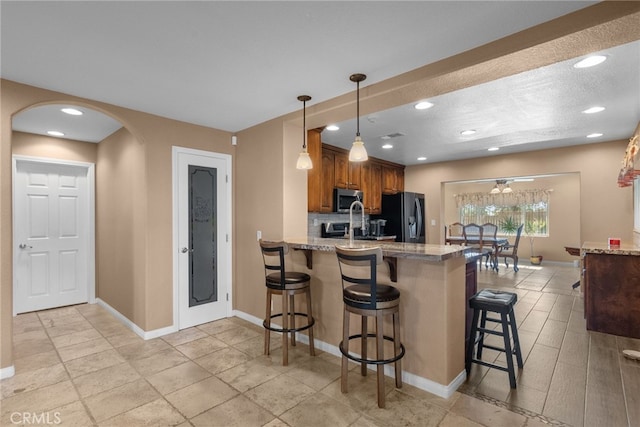40139 15th St W, Palmdale, CA 93551 - kitchen featuring stainless steel microwave, black fridge with ice dispenser, a breakfast bar area, a peninsula, and brown cabinets