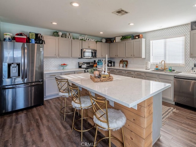 3031 E Lingard St, Lancaster, CA 93535 - kitchen featuring stainless steel appliances, backsplash, a center island, a kitchen bar, and dark wood finished floors