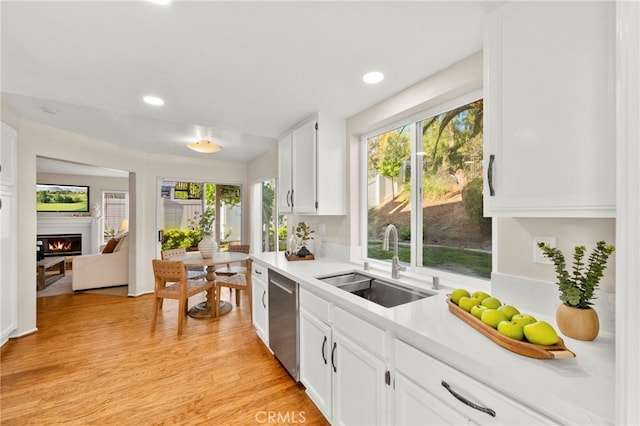 41024 Montelena Cir, Temecula, CA 92591 - kitchen with stainless steel dishwasher, white cabinets, light countertops, light wood-style flooring, and a glass covered fireplace