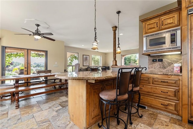 9942 Sunfish Cir, Paso Robles, CA 93446 - kitchen featuring stainless steel microwave, stone tile floors, a breakfast bar area, brown cabinetry, and ceiling fan