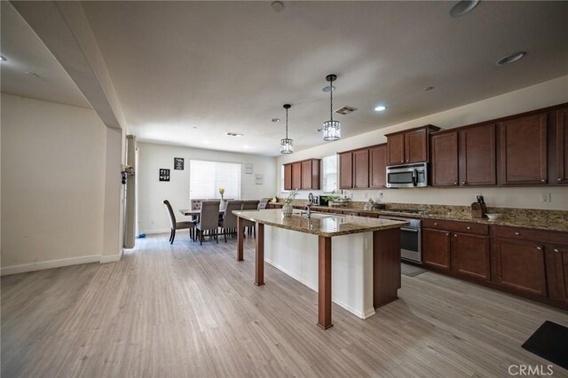 15930 Chorus Ln, Fontana, CA 92336 - kitchen with stainless steel microwave, light wood-style flooring, a breakfast bar area, an island with sink, and recessed lighting