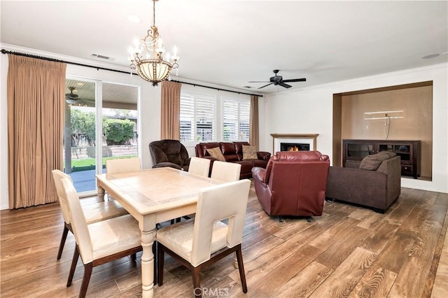 26865 Shelter Cove Ct, Menifee, CA 92585 - dining area with a ceiling fan, ornamental molding, wood finished floors, a chandelier, and a lit fireplace