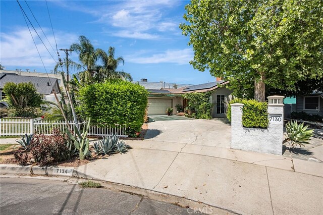 7134 Stansbury Ave, Van Nuys, CA 91405 - view of property hidden behind natural elements with driveway, solar panels, and an attached garage