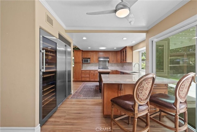 5706 E Bryce Ave, Orange, CA 92867 - kitchen featuring stainless steel microwave, brown cabinets, a peninsula, crown molding, and backsplash