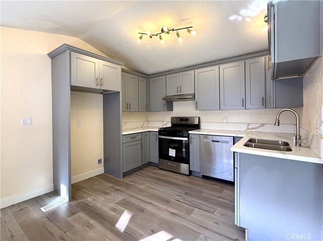 1639 Winn Ct, Pomona, CA 91768 - kitchen with stainless steel appliances, gray cabinetry, under cabinet range hood, lofted ceiling, and light wood finished floors