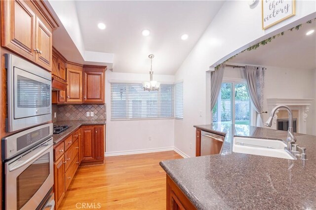 24302 Vista Ridge Dr, Valencia, CA 91355 - kitchen featuring appliances with stainless steel finishes, a chandelier, light wood finished floors, brown cabinets, and backsplash