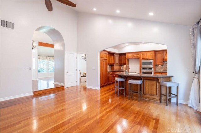 24302 Vista Ridge Dr, Valencia, CA 91355 - kitchen featuring appliances with stainless steel finishes, arched walkways, brown cabinets, light wood-style flooring, and a ceiling fan