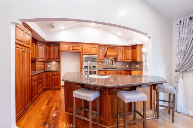 24302 Vista Ridge Dr, Valencia, CA 91355 - kitchen with stainless steel appliances, vaulted ceiling, brown cabinetry, light wood-type flooring, and tasteful backsplash