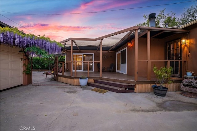 7028 E Parkcrest St, Long Beach, CA 90808 - back of house at dusk featuring a wooden deck, a patio, stucco siding, and a garage