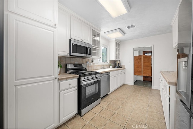 7028 E Parkcrest St, Long Beach, CA 90808 - kitchen with appliances with stainless steel finishes, tile countertops, white cabinets, and decorative backsplash