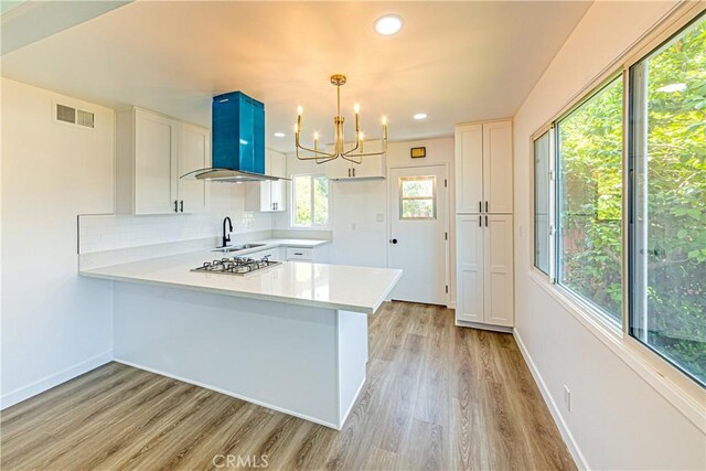 1510 W 147th St, Gardena, CA 90247 - kitchen with wall chimney exhaust hood, light countertops, a peninsula, stainless steel gas stovetop, and white cabinets