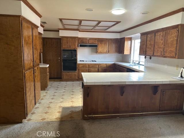 27208 Cornell St, Hemet, CA 92544 - kitchen with a peninsula, black appliances, under cabinet range hood, tile countertops, and crown molding