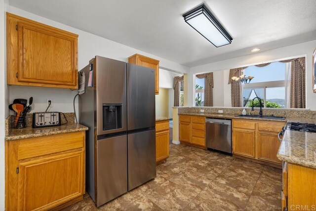 4722 Regatta Ln, San Diego, CA 92154 - kitchen with stainless steel appliances, a chandelier, brown cabinetry, light stone counters, and recessed lighting