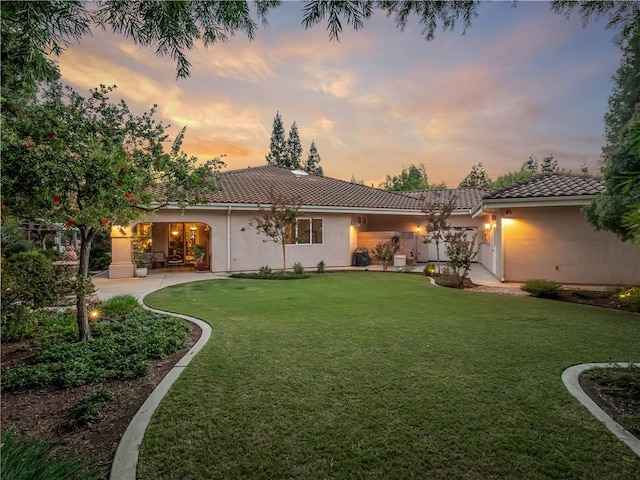 6660 N St Catherine Ct, Fresno, CA 93711 - back of property at dusk featuring a tiled roof, a lawn, and stucco siding