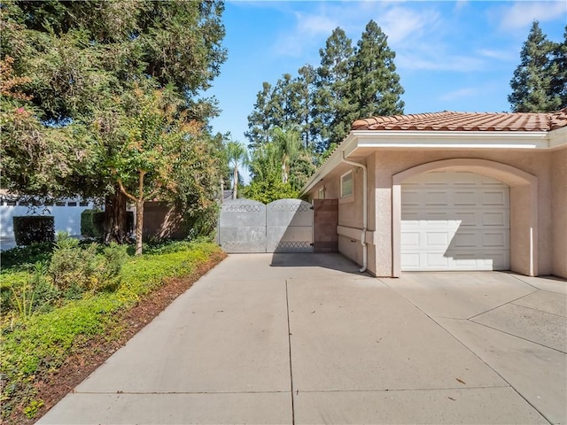 6660 N St Catherine Ct, Fresno, CA 93711 - view of side of home with concrete driveway, a gate, a garage, stucco siding, and a tiled roof