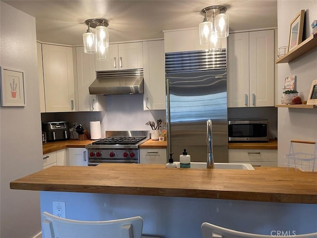 3641 S Bear St Unit F, Santa Ana, CA 92704 - kitchen with wooden counters, appliances with stainless steel finishes, under cabinet range hood, white cabinets, and a breakfast bar