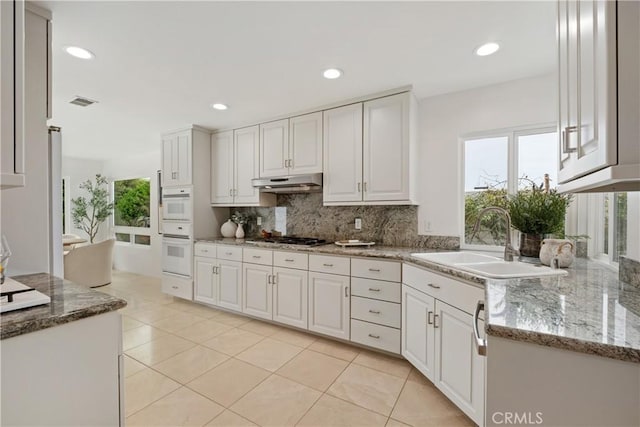 32512 Seven Seas Dr, Dana Point, CA 92629 - kitchen with backsplash, white cabinetry, under cabinet range hood, light tile patterned floors, and light stone countertops