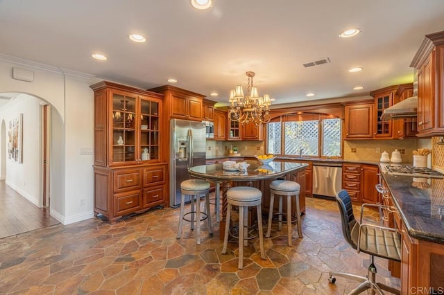 4280 Trias St, San Diego, CA 92103 - kitchen with stainless steel appliances, a chandelier, arched walkways, brown cabinetry, and wall chimney range hood